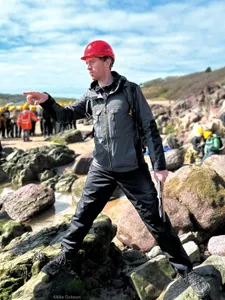 a man in a red hard hat pointing at some rocks, explaining something