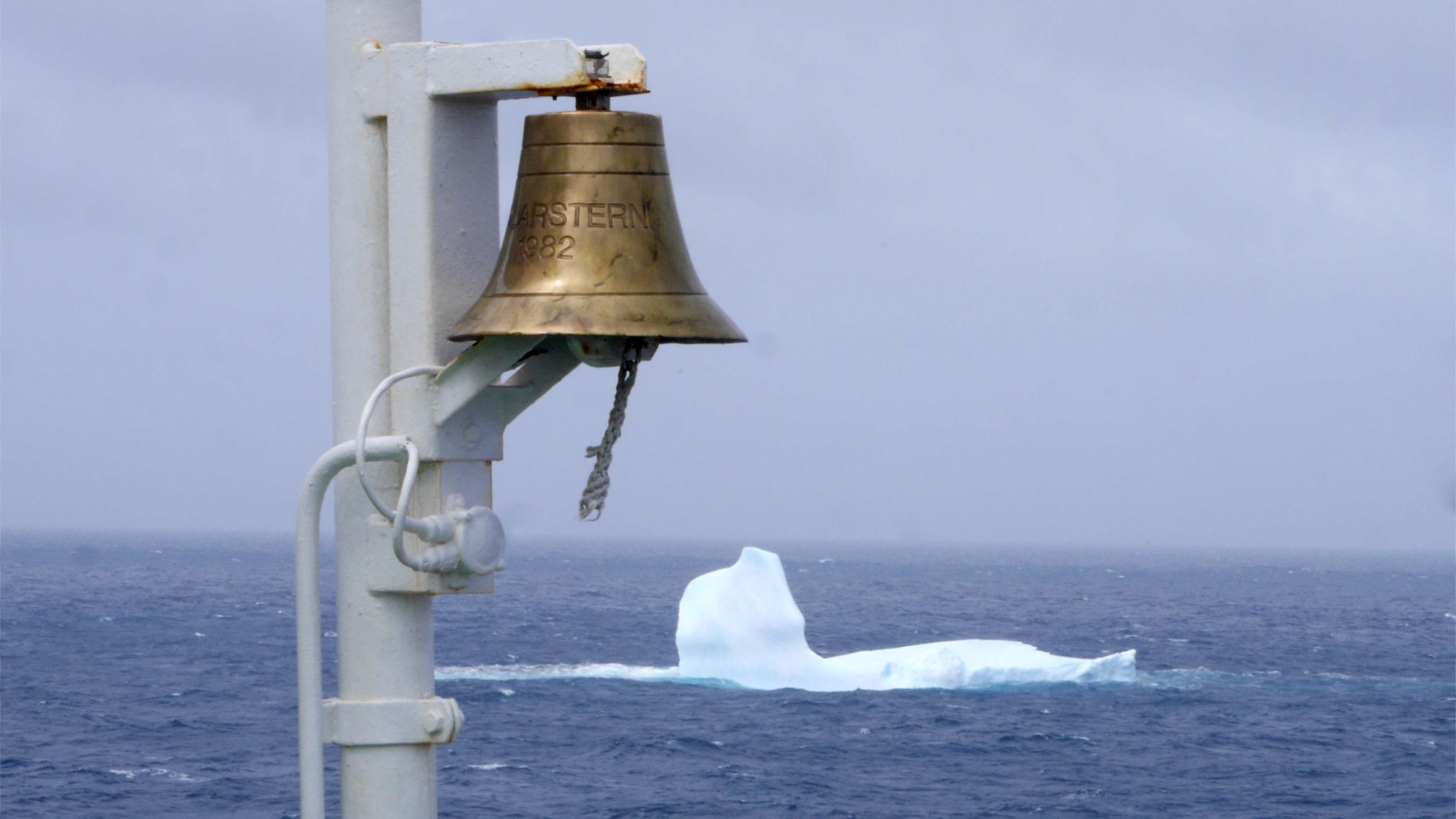 An iceberg in a grey ocean. The iceberg has the rough outline of a bird lying on its back.