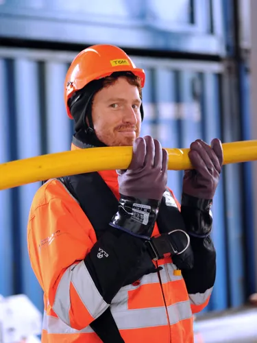 A man in orange hi-vis clothing holding a yellow pipe.