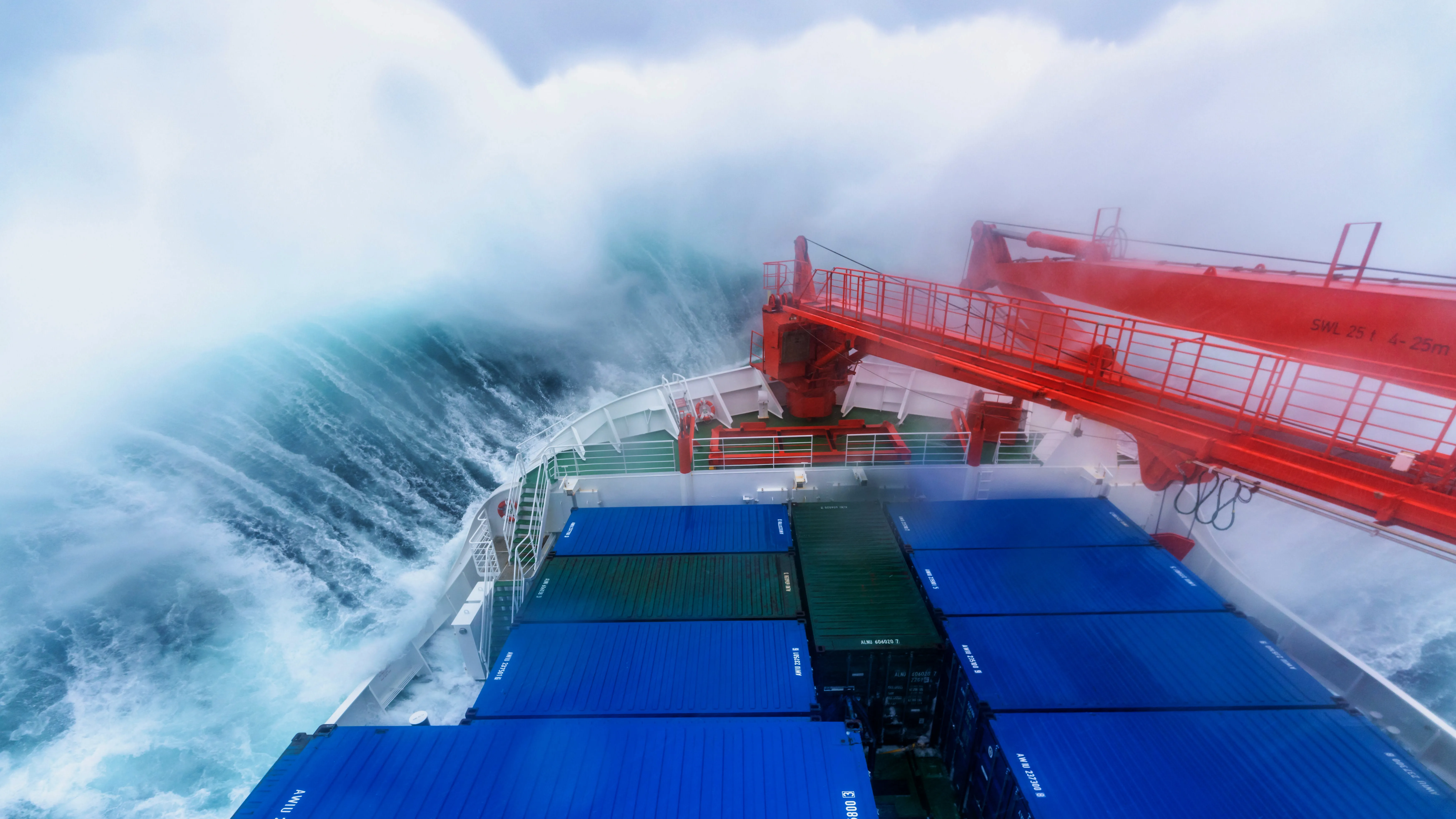 Viewed from the bridge, the bow of a ship smashes into a huge wave, sending streaks of spray away on both sides