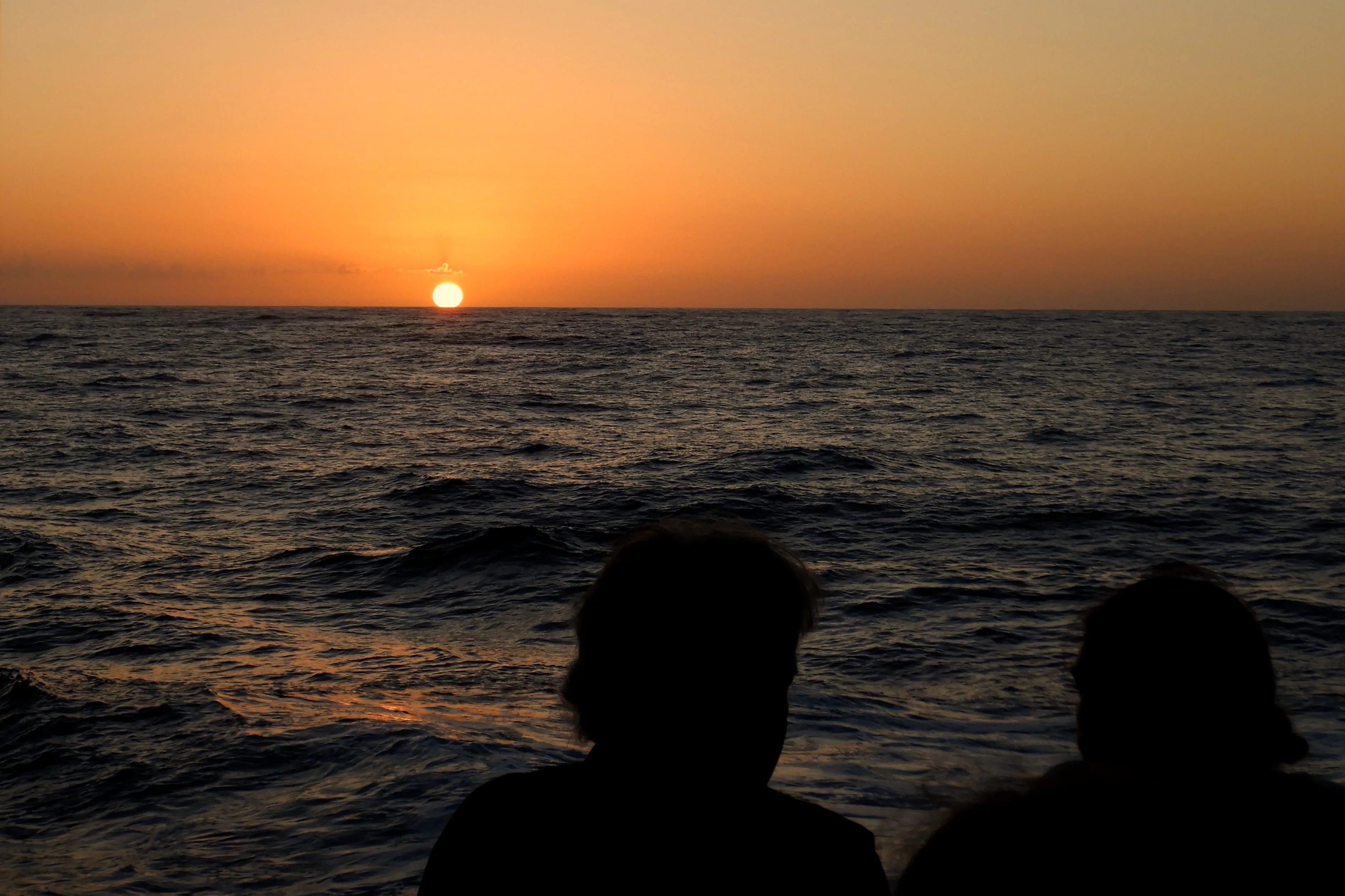 A sunset at sea with the silhouettes of two people watching